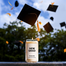 A lifestyle image of the New Grad Homesick candle in an outdoor environment surrounded by falling graduation caps.