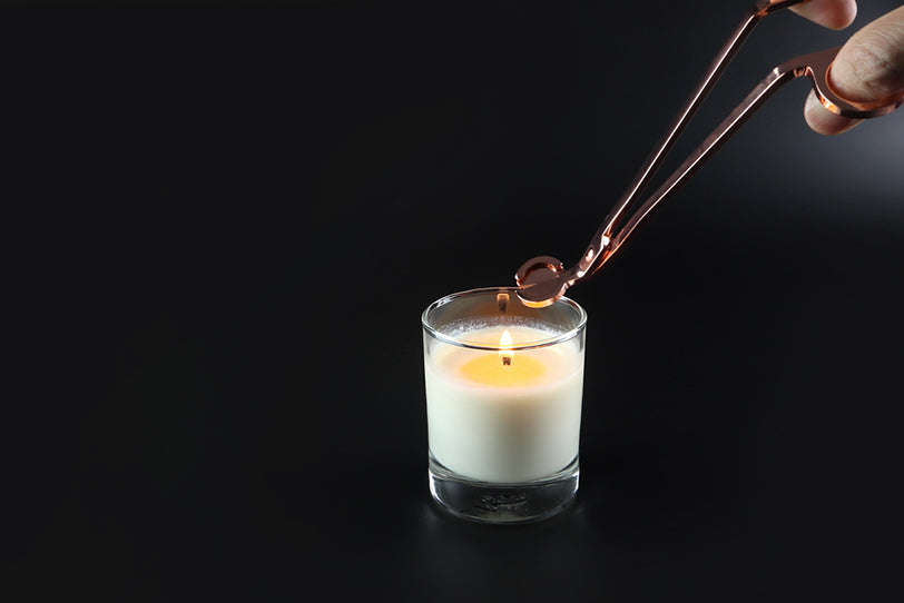 a person using a wick trimmer on a scented candle on a table