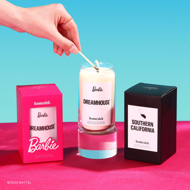 A group shot of the products in the Malibu Barbie Bundle: the Dreamhouse and Southern California candles. Shot on a pink surface and light blue background.