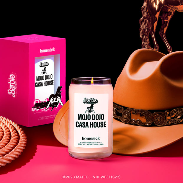 A graphic showing the Mojo Dojo Casa House Candle in front of a brown cowboy hat and the packaging for the candle.