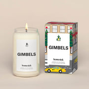 A lit Elf Gimbels Homesick candle displayed next to its boxed packaging on a dark cream background.