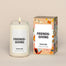 A lit Friendsgiving Homesick candle displayed next to its boxed packaging on a dark cream background.
