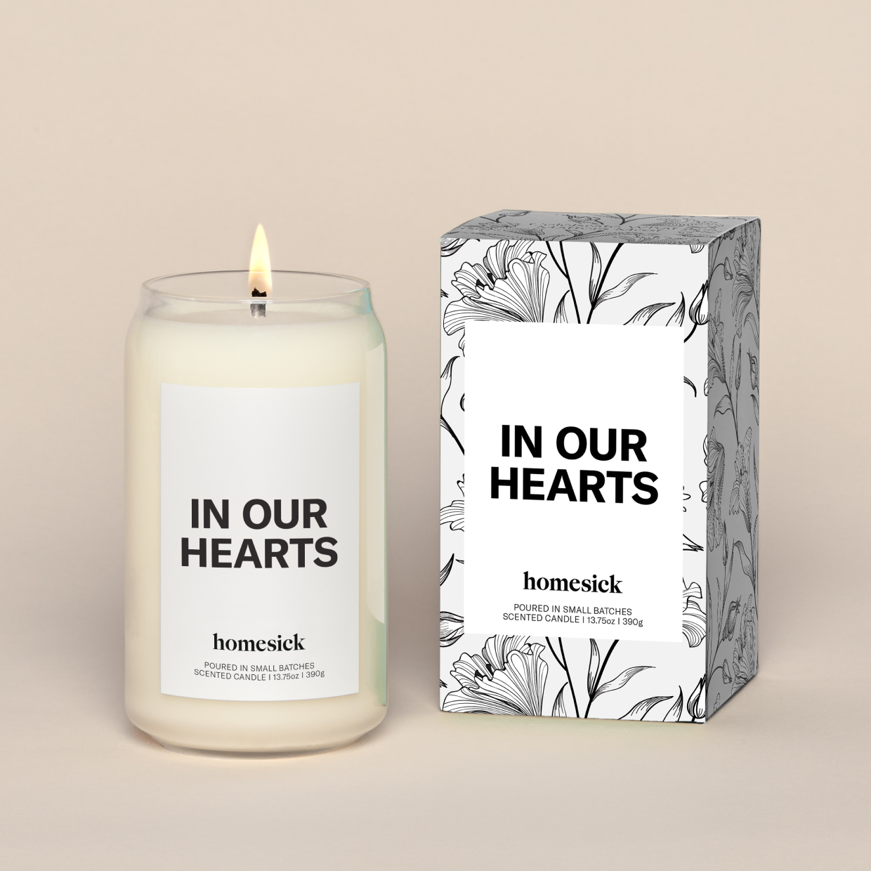 A lit In Our Hearts Homesick candle displayed next to its boxed packaging on a dark cream background.