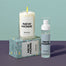 A group shot showing the New Bundle products. The New Home candle is displayed on top of it's boxed packaging that is laying down sideways. To the right of that is the New Home Room Spray. Both items displayed on a grayish blue surface with a mint green background. 