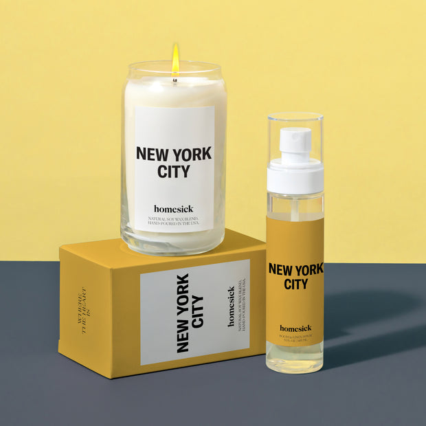 A group product shot of the New York City Candle and New York City Linen Spray. The candle is displayed on top of its boxed packaging that is laying down sideways. 
