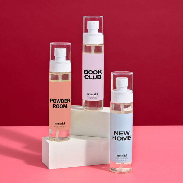 A group shot of three home inspired room sprays shot on a pink surface with a red background.
