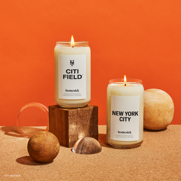 A group shot of New York Mets inspired candles from Homesick shot on a corkboard like surface with a burnt orange background.