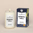 A lit Spiral Hill Homesick candle displayed next to its boxed packaging on a dark cream background.