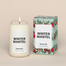 A lit Winter MantelHomesick candle displayed next to its boxed packaging on a dark cream background.