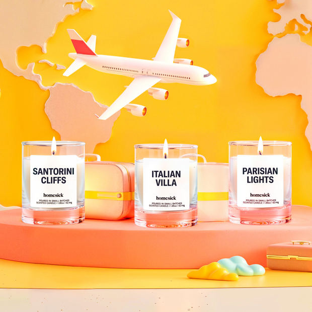 Lifestyle image of three mini candles labelled "Sanitorini Cliffs", "Italian Villa", and "Parisian Lights" in a travel setting as a passenger plane flies overhead