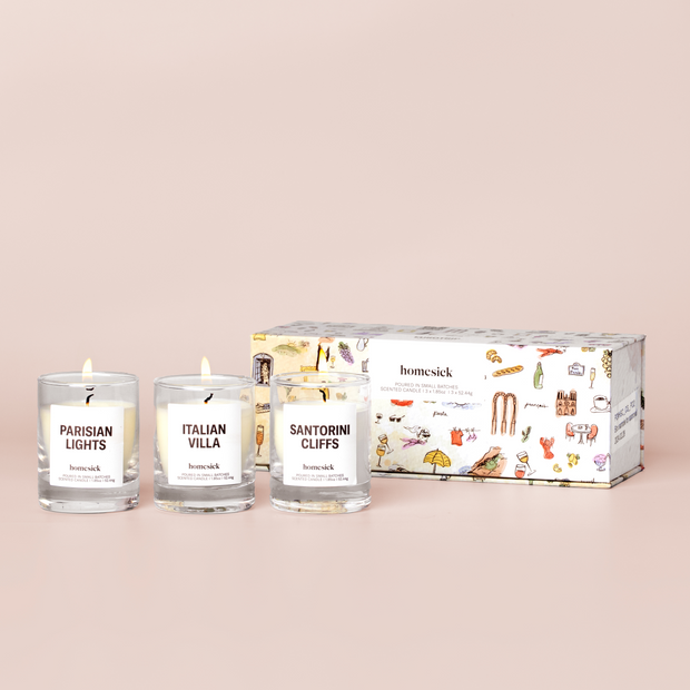 three mini candles labelled "Sanitorini Cliffs", "Italian Villa", and "Parisian Lights" and a box on a cream background