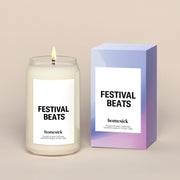 A lit Festival Beats Homesick candle displayed next to its boxed packaging on a dark cream background.