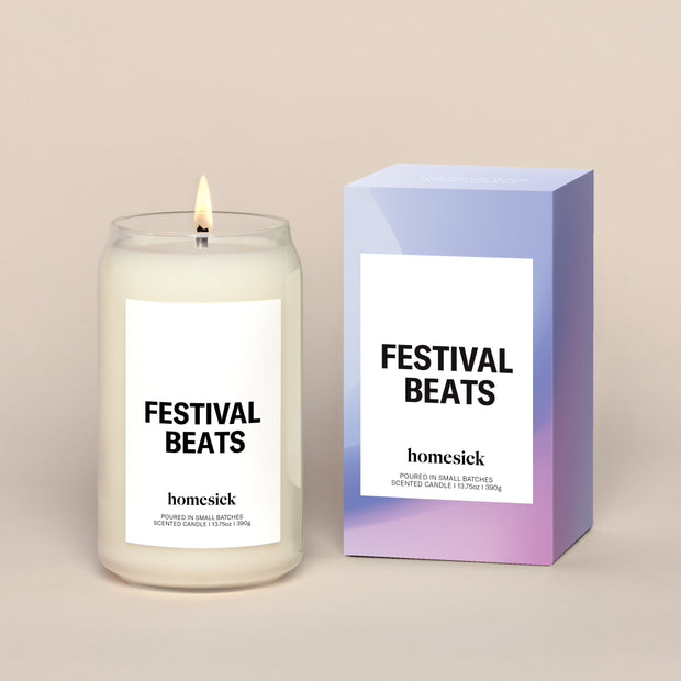 A lit Festival Beats Homesick candle displayed next to its boxed packaging on a dark cream background.