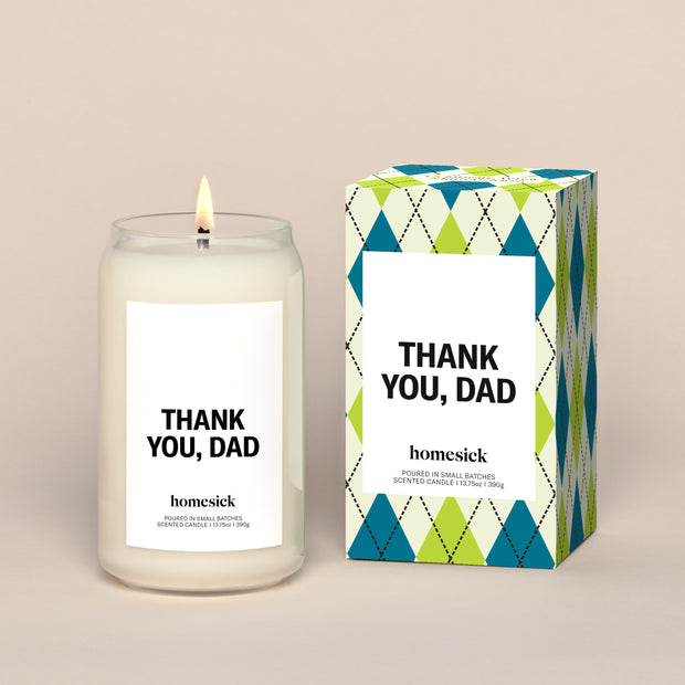 A lit Thank You, Dad Homesick candle displayed next to its boxed packaging on a dark cream background.