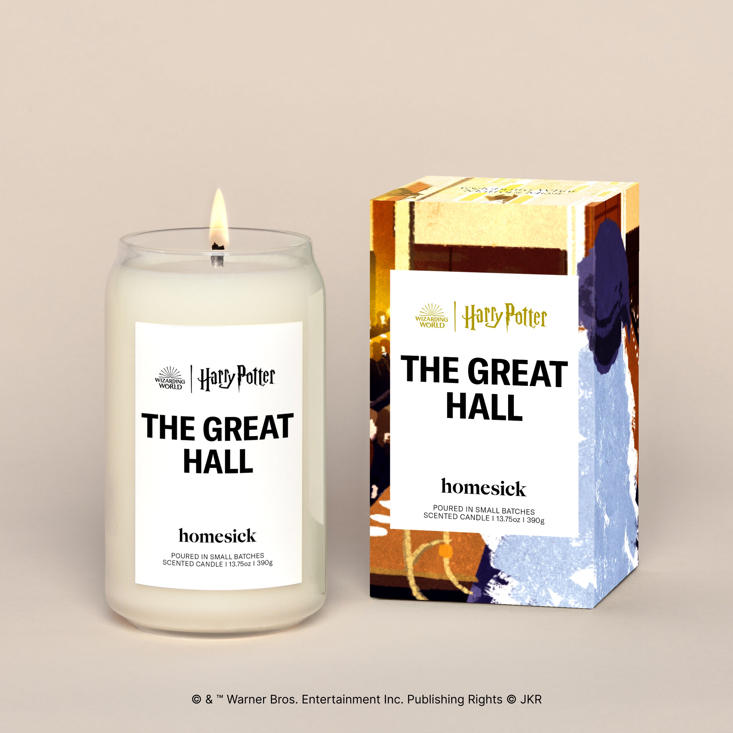 A lit The Great Hall candle displayed next to its boxed packaging on a dark cream background.