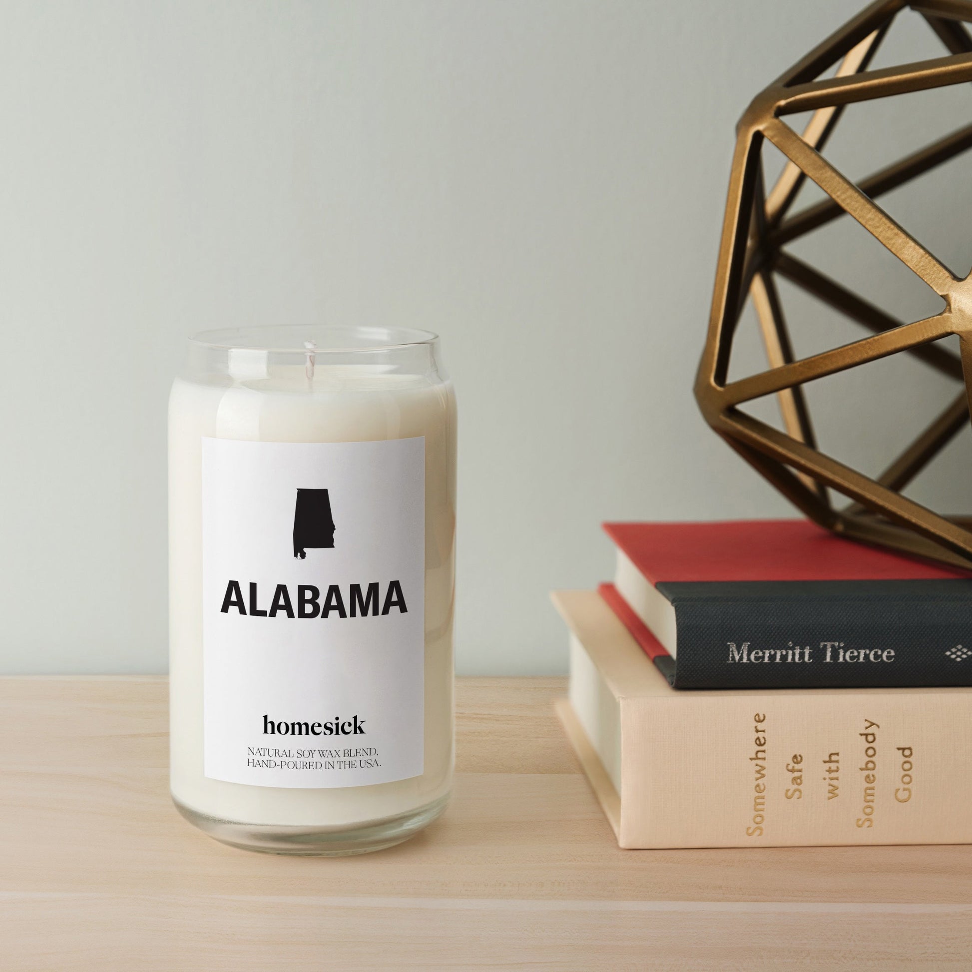 A close up of the Alabama Homesick Candle on a table next to a stack of books.
