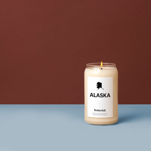 A lit Alaska Candle on top of a blue surface with a brown background.