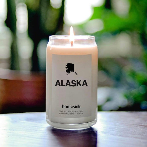 A close up of a lit Alaska Candle. The background is blurred greenery.