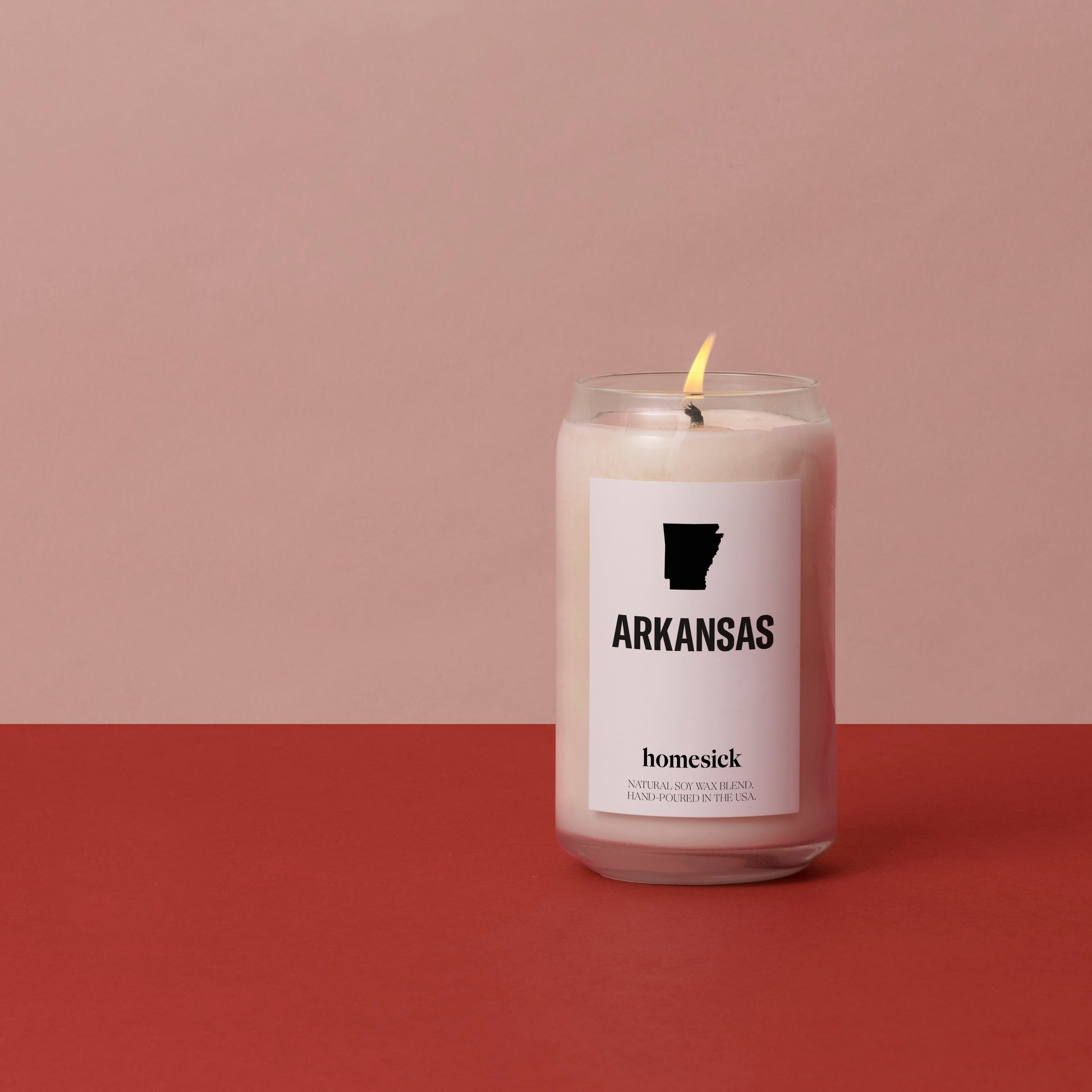 A lit Arkansas candle displayed on a red background with a salmon pink background.