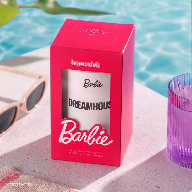 The packaged Barbie Dreamhouse Candle propped poolside with various pool props in the corners.