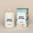 A lit Beach Cottage Homesick candle displayed next to its boxed packaging on a dark cream background.