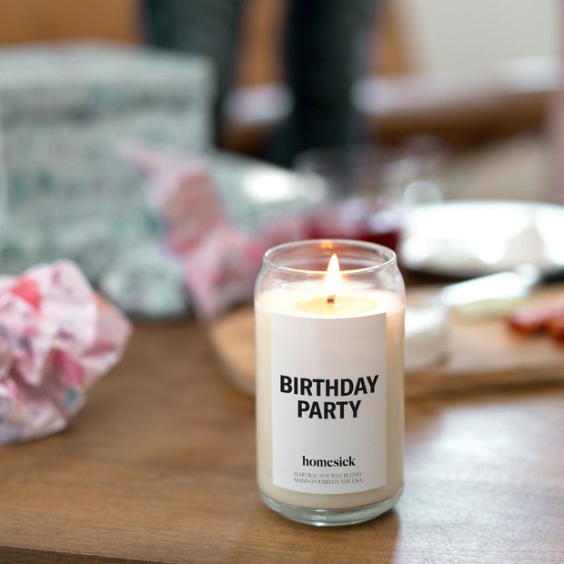 A lifestyle image of the lit Birthday Party Candle on a wooden table where the background is blurred.