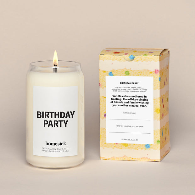 A lit Birthday Party Homesick candle displayed next to its boxed packaging on a dark cream background.