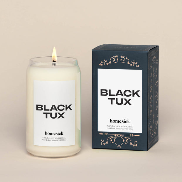 A lit Black Tux Homesick candle displayed next to its boxed packaging on a dark cream background.