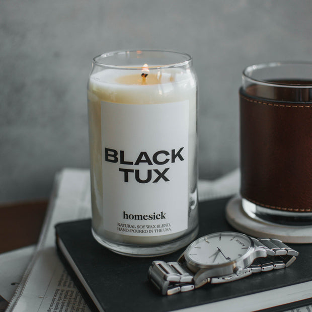 A close up image of the Black Tux candle displayed on top of a black notebook with other men's small items around it as props.