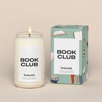 A lit Book Club Homesick candle displayed next to its boxed packaging on a dark cream background.