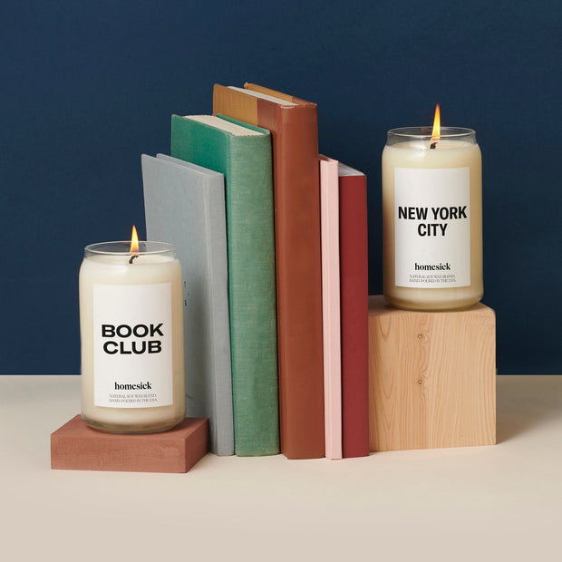 Two homesick candles used as book ends for a stack of books.
