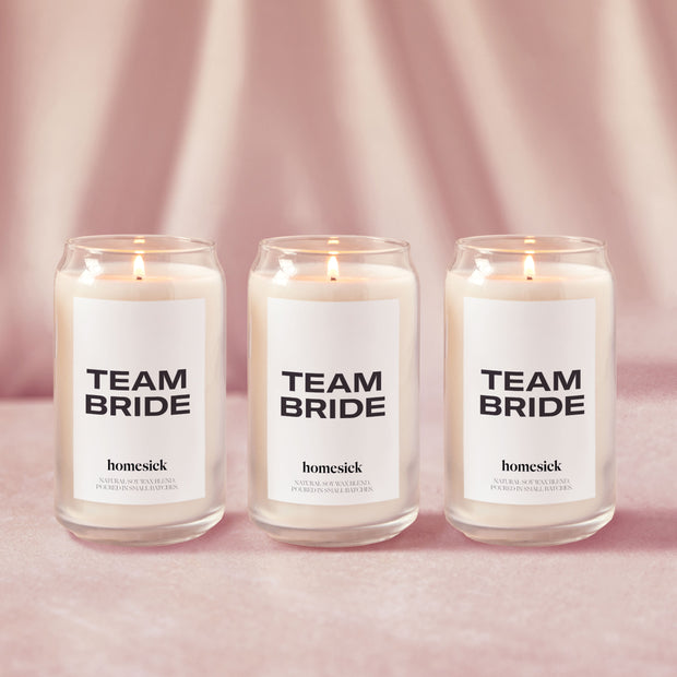 Three Team Bride Candles lined up next to each other shot on a light pink surface with a silky pink background.