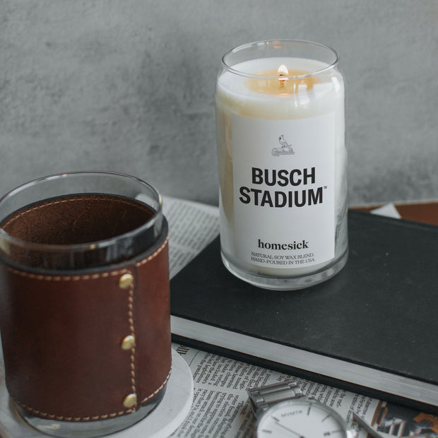 A Busch Stadium candle on top of a black notebook with various men's items around that.