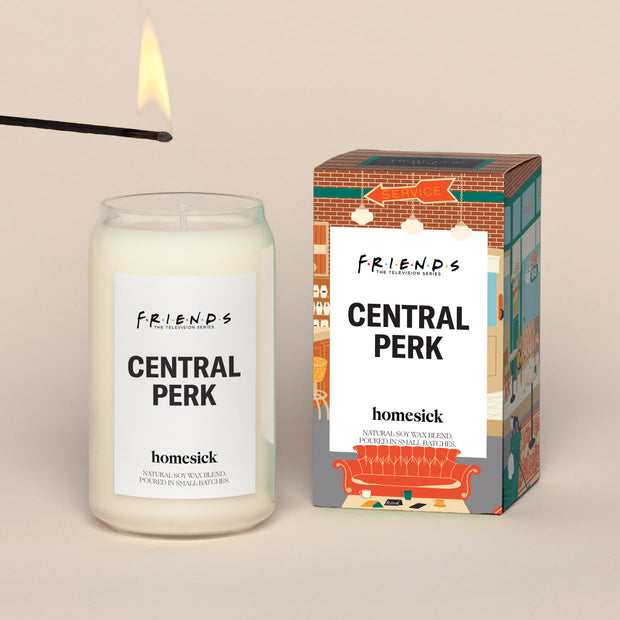 A lit Central Park Homesick candle displayed next to its boxed packaging on a dark cream background.