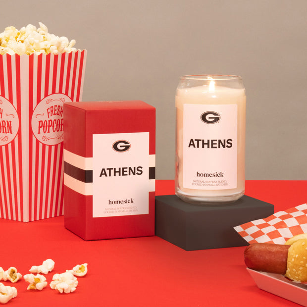 A lit Athens Georgia candle lit next to its boxed packaging. There are various tailgating props are it for the Georgia Bull dogs.