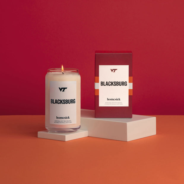 A colorful display of the VT Blacksburg candles on a white pedestals with an orange surface and red background.
