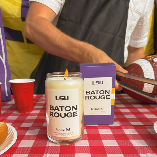 The LSU Baton Rouge candle lit at tailgate on top of a checkered picnic tablecloth.
