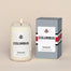 A lit Columbus Homesick candle displayed next to its boxed packaging on a dark cream background.