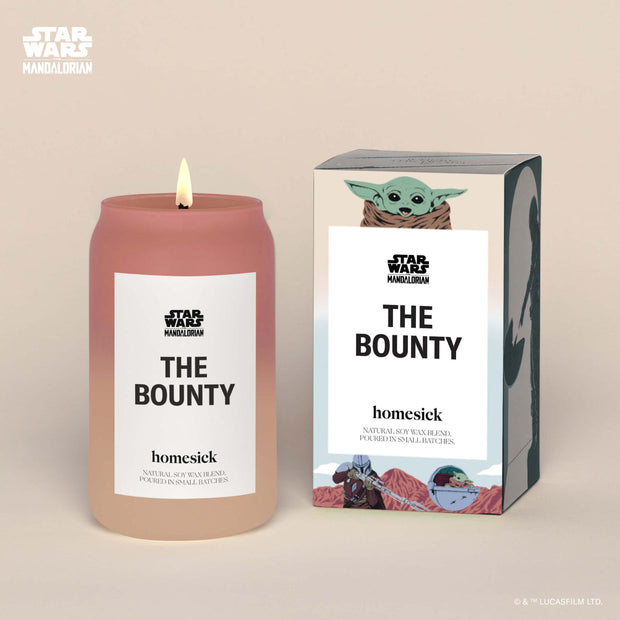 A lit "The Bounty" Homesick candle displayed next to its boxed packaging on a dark cream background.