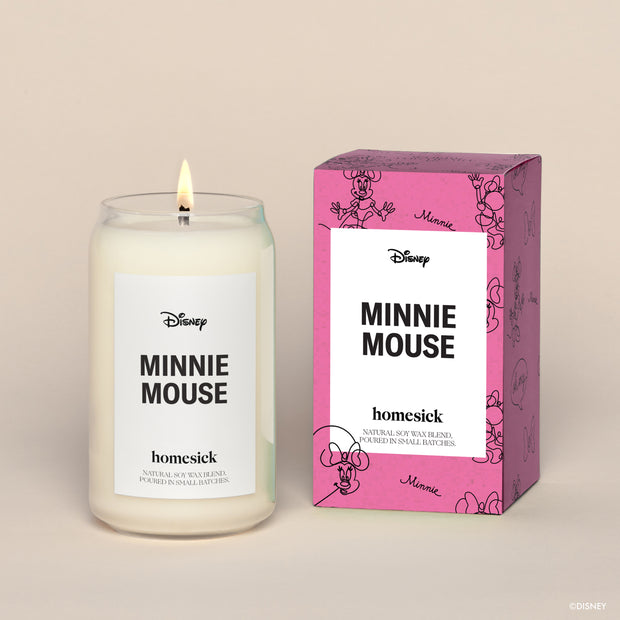 A lit Minnie Mouse Homesick candle displayed next to its boxed packaging on a dark cream background.
