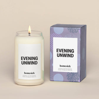 Single evening unwind lit candle next to a purple box, which the candle comes in. 