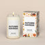 A lit Autumn Hayride Homesick candle displayed next to its boxed packaging on a dark cream background.