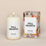 A lit Fall Hearth Homesick candle displayed next to its boxed packaging on a dark cream background.