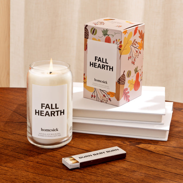 A Fall Hearth Candle and its packaging displayed on a wooden table.