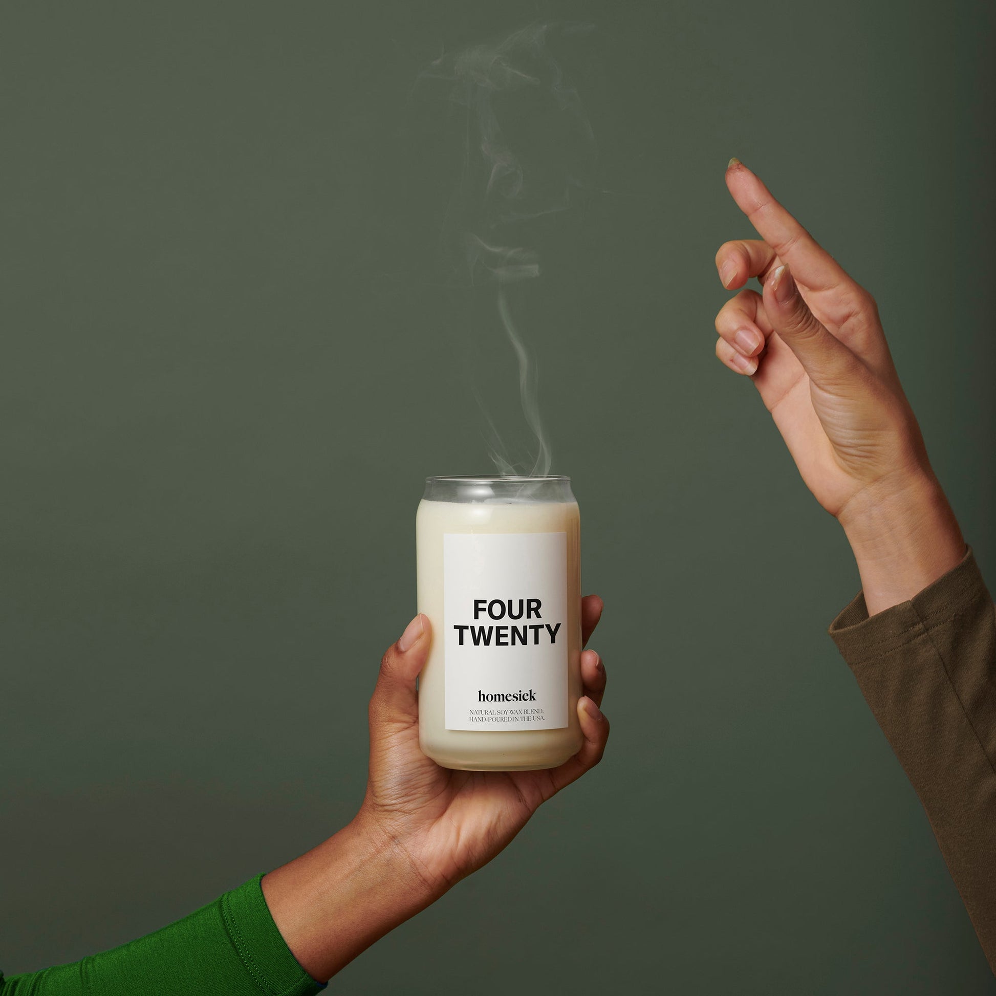 Someone holding the Four Twenty Candle with another hand moving away that just pinched the candle wick.