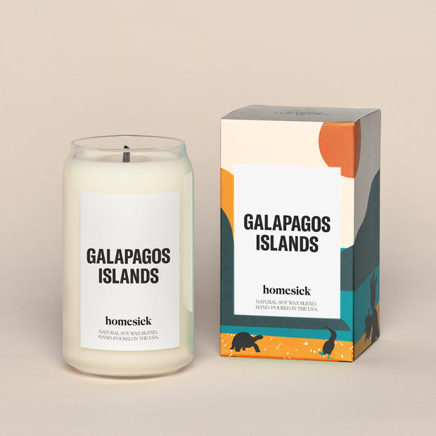 A lit Galapagos Islands Homesick candle displayed next to its boxed packaging on a dark cream background.
