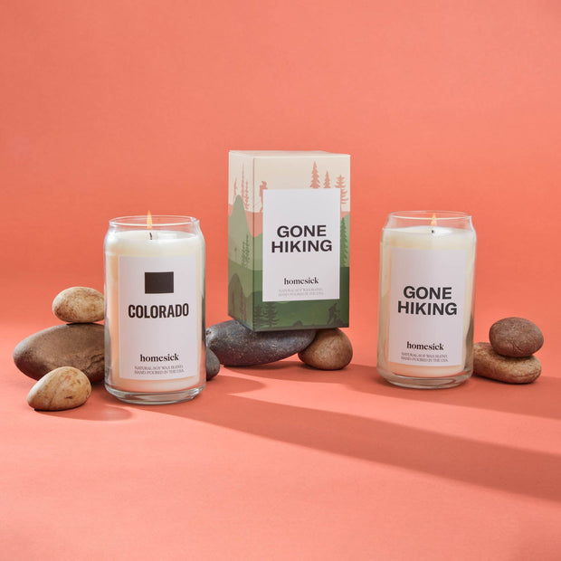 The Colorado and Gone Hiking homesick candles shot inside a salmon pink environment. There are rocks around the candles for props.