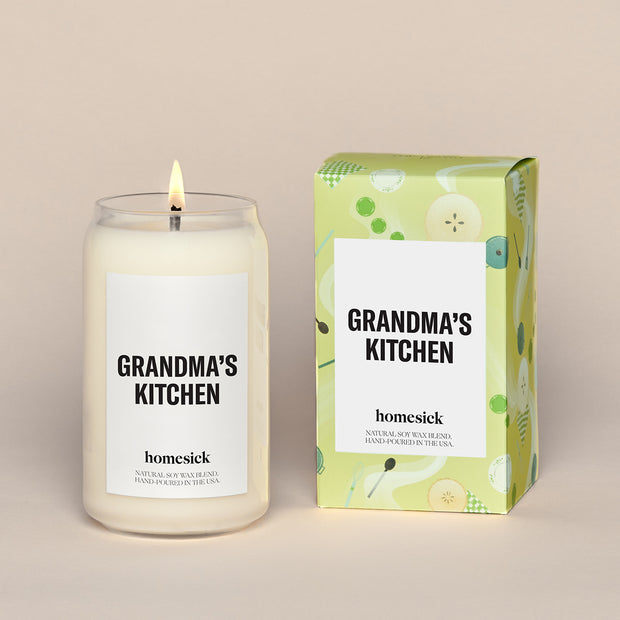 A lit Grandma's Kitchen Homesick candle displayed next to its boxed packaging on a dark cream background.