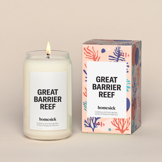 A lit Great Barrier Reef Homesick candle displayed next to its boxed packaging on a dark cream background.