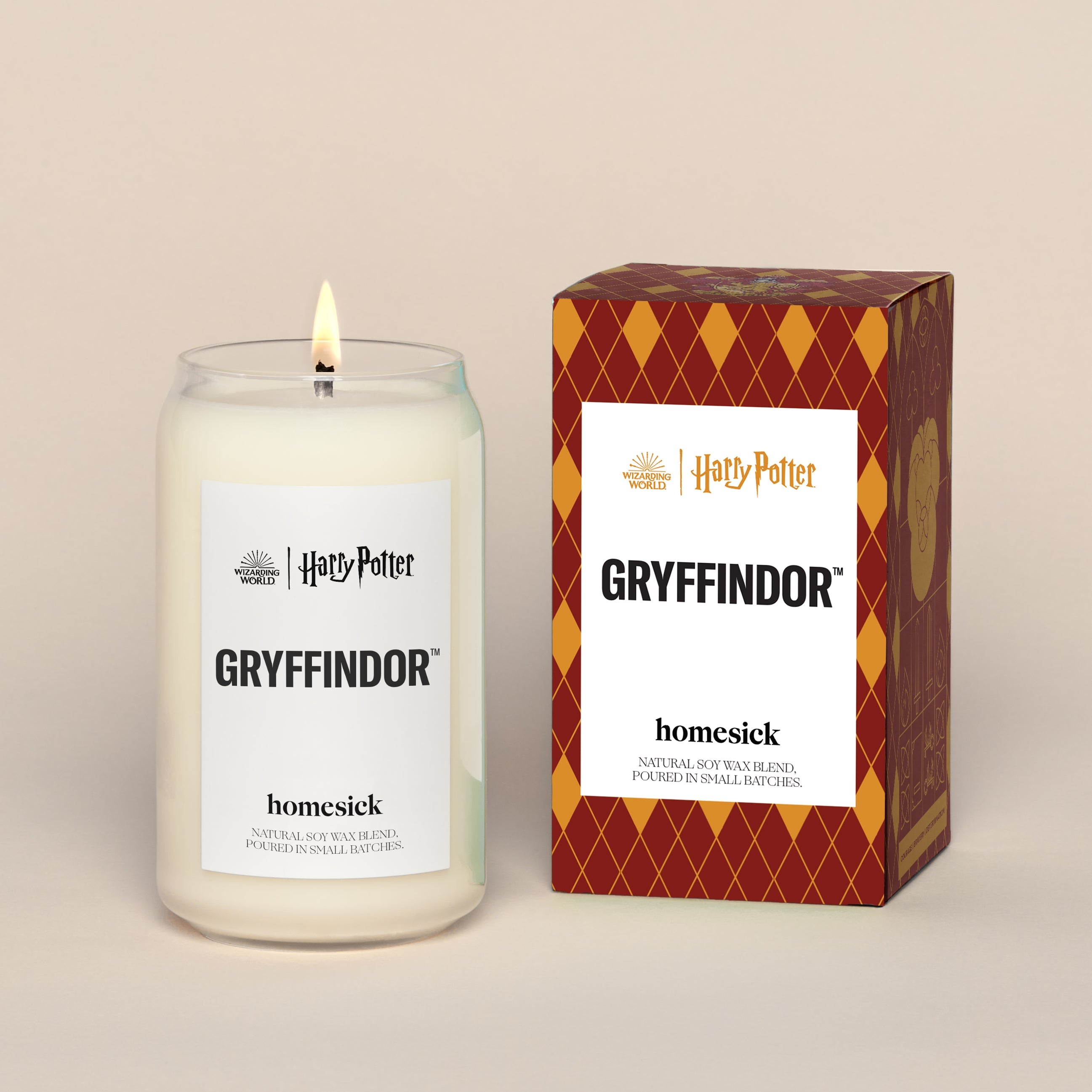 A lit Gryffindor Homesick candle displayed next to its boxed packaging on a dark cream background.
